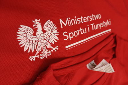 Wyraźnie drobne elementy godła Polski. Na czerwonej poliestrowej - sportowej koszulce.